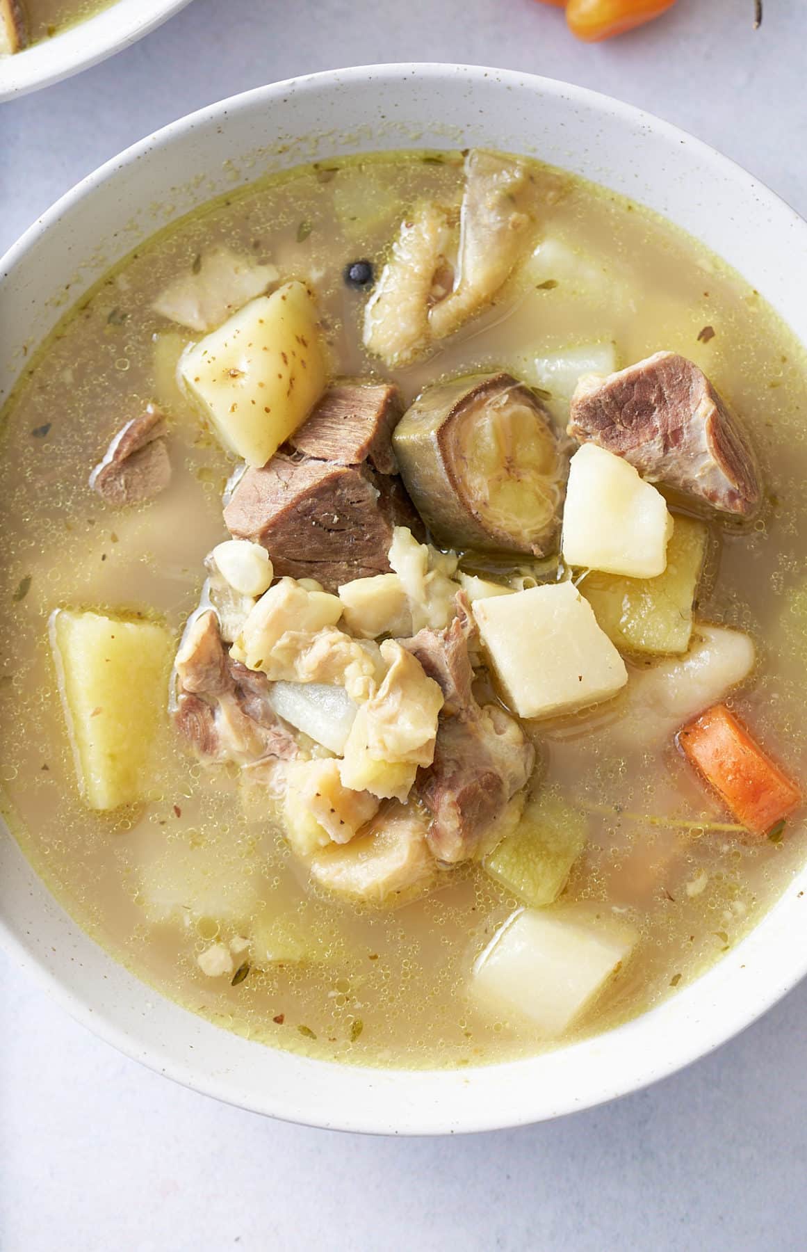 White bowl filled with goat, tripe and vegetable soup.