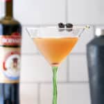 A bourbon martini cocktail in a cocktail glass served with two cocktail cherries, with a bottle of bourbon and cocktail shaker in the background.