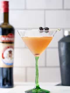 A bourbon martini cocktail in a cocktail glass served with two cocktail cherries, with a bottle of bourbon and cocktail shaker in the background.