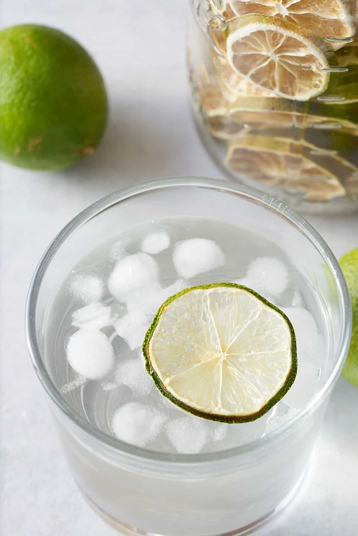 glass of water with ice with dried lime on top and dried limes in background