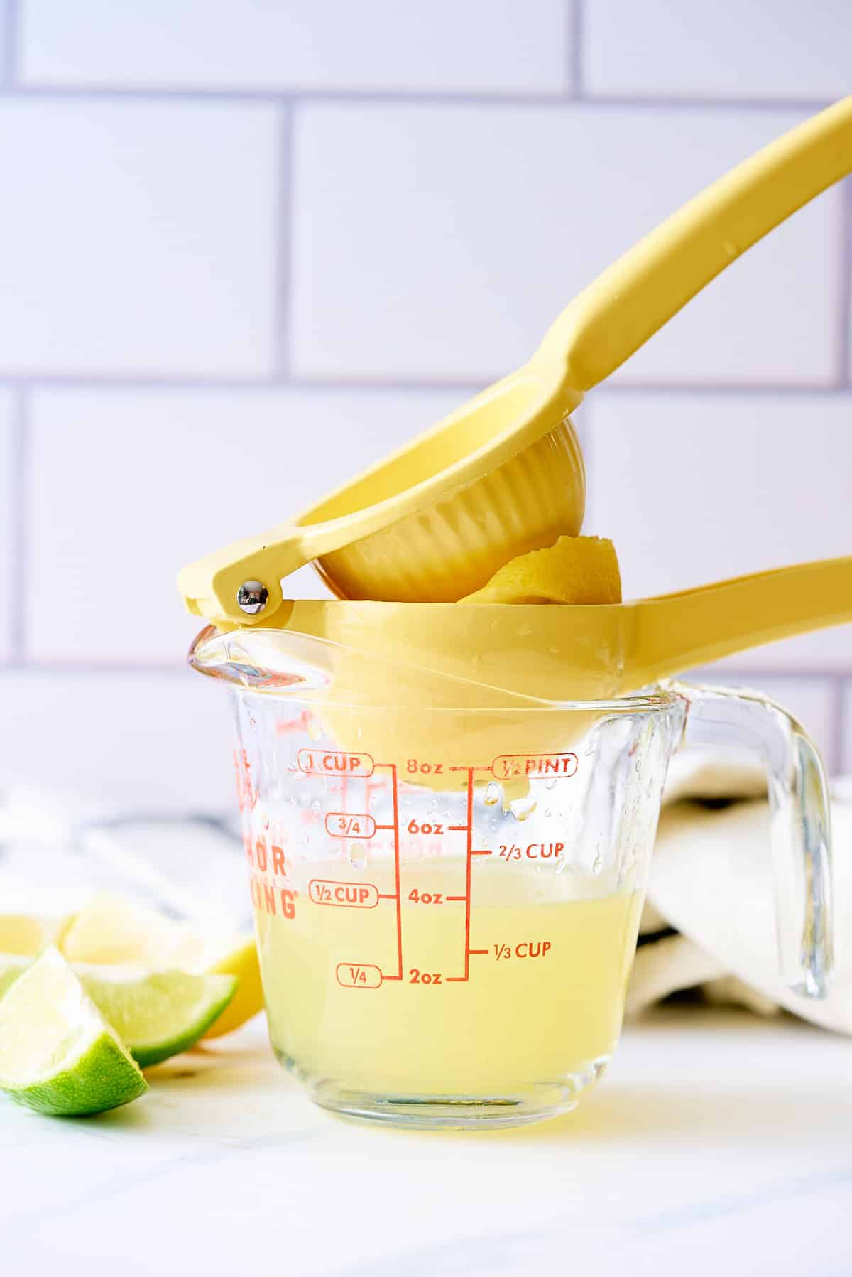 A hand held lemon press squeezing fresh lemon juice into a glass jug.