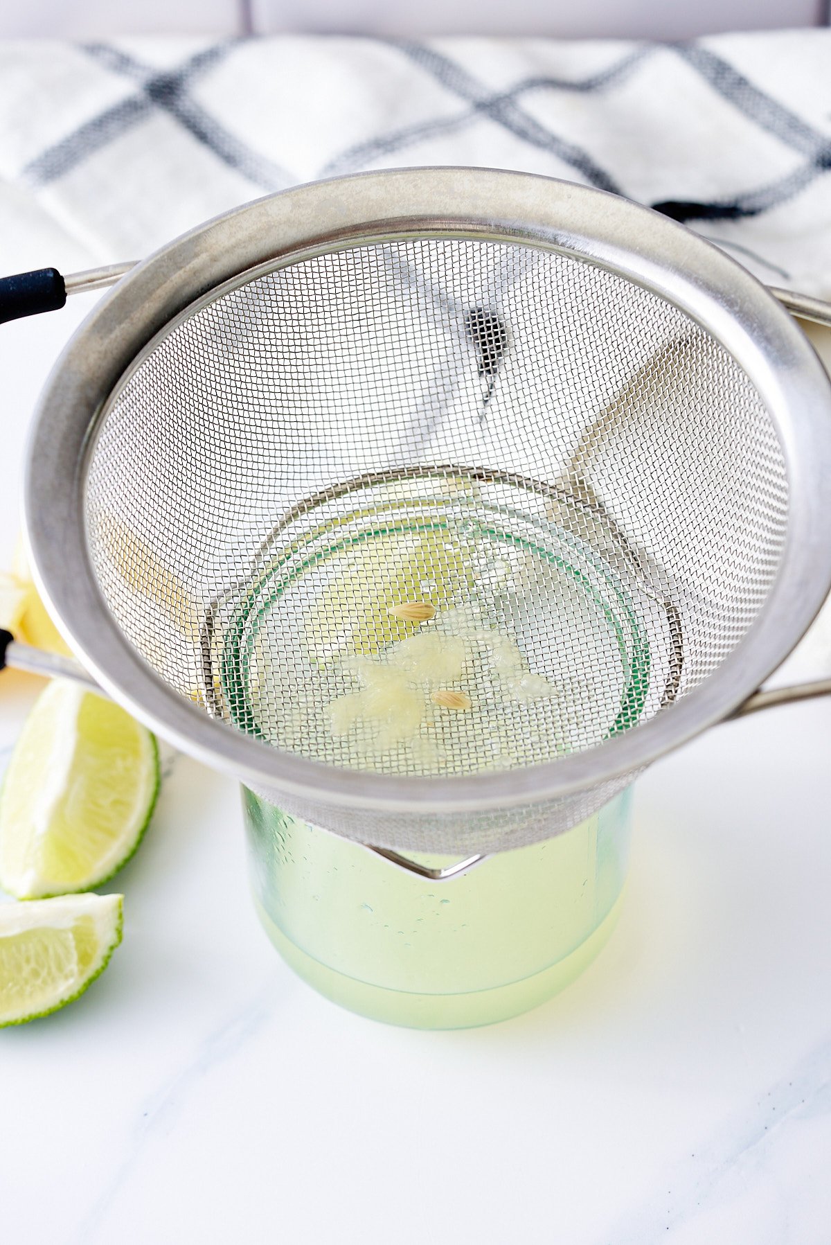 Lemon and lime juice being passed through a fine sieve into a glass jug.
