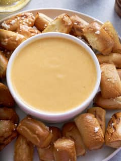 beer cheese dip in white bowl with pretzels surrounding it