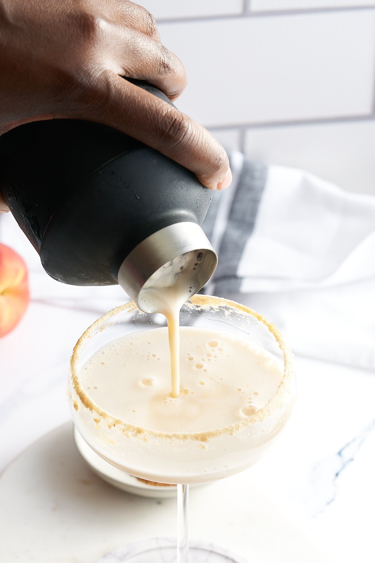 Peach cobbler cocktail being sieved through a cocktail shaker into a cocktail glass.