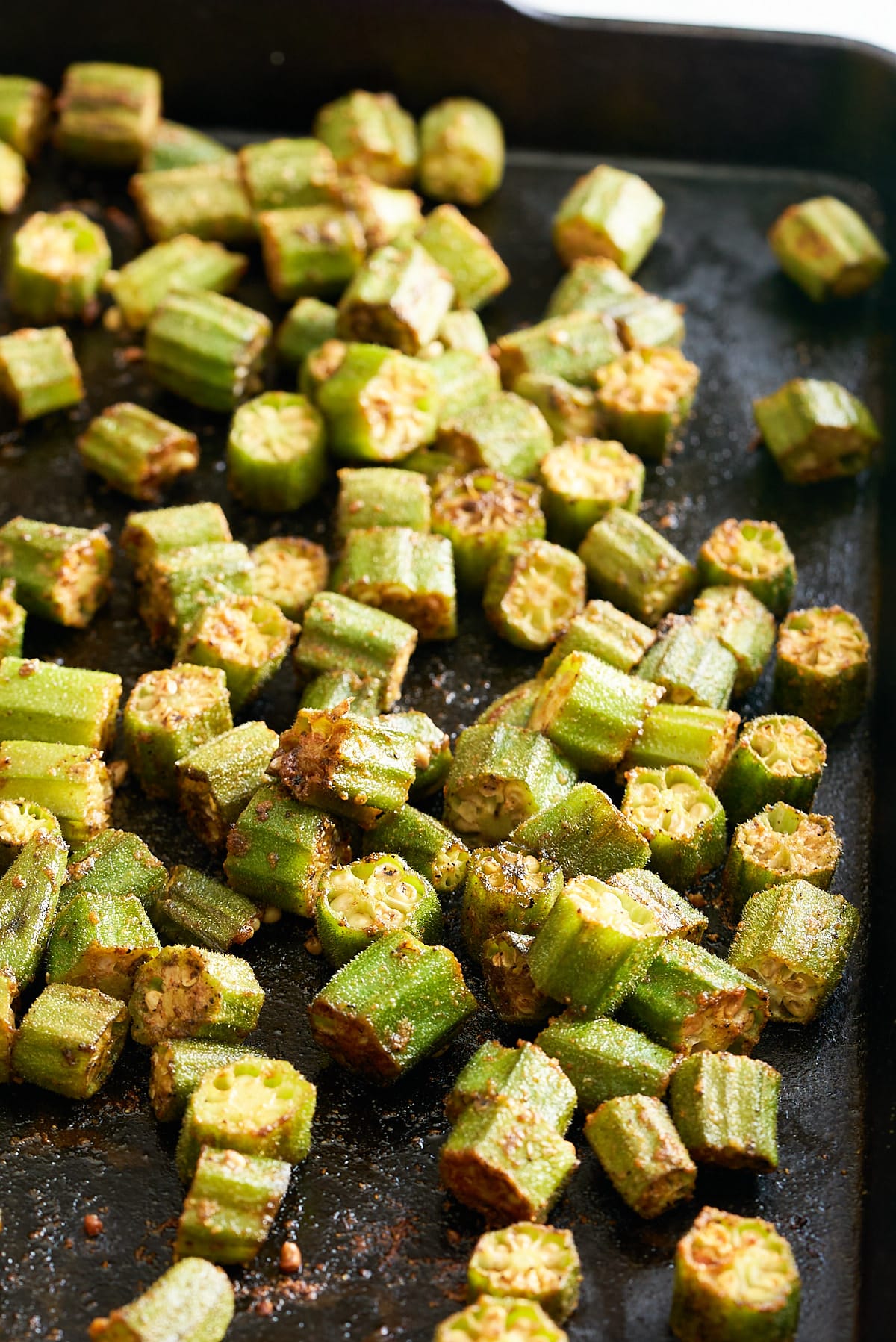 An oven proof baking sheet with pieces of spiced okra spread over.