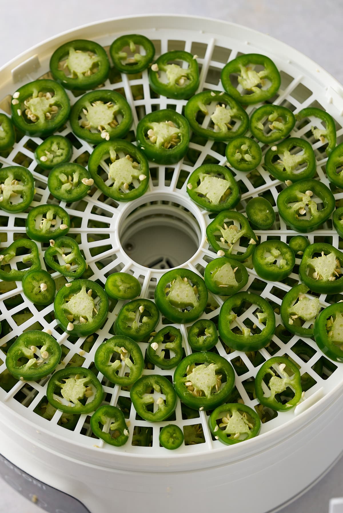 Sliced jalapenos spread around on a dehydrator.