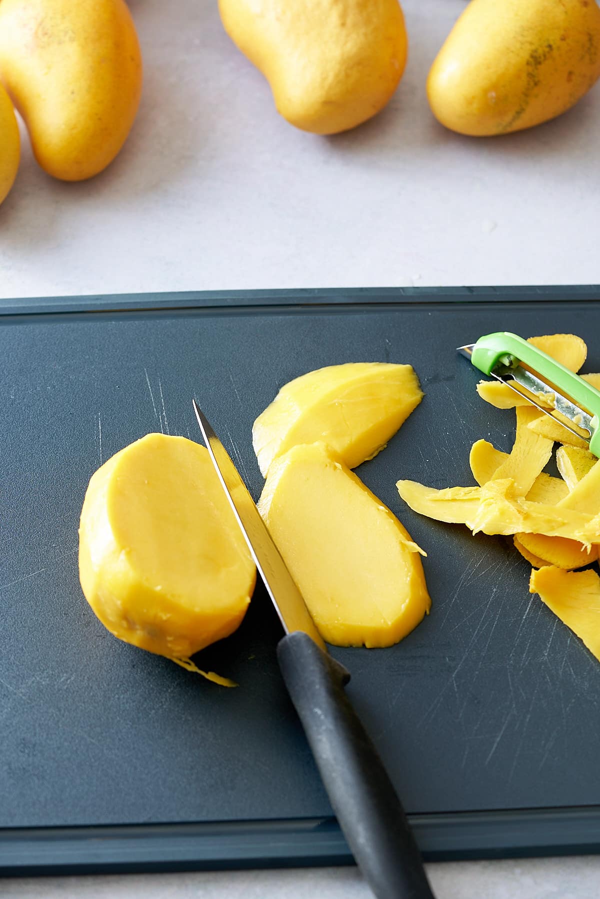 mango being sliced with knife on black cutting board