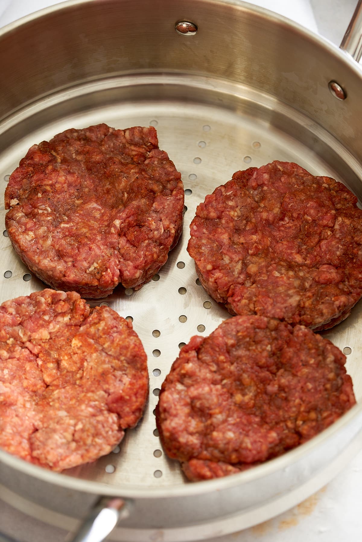 Raw beef patties placed into a steamer.