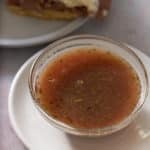 A glass bowl filled with au jus with some roast beef sliders set alongside.