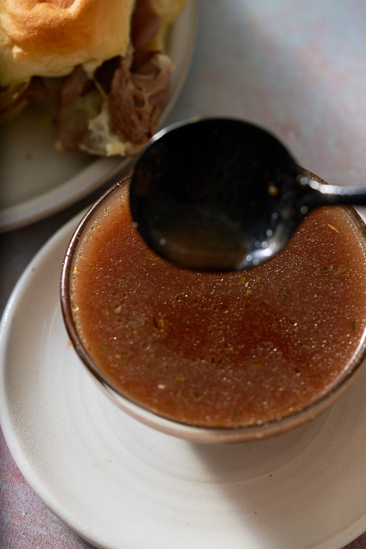 A glass bowl filled with au jus and a roast beef slider set alongside.