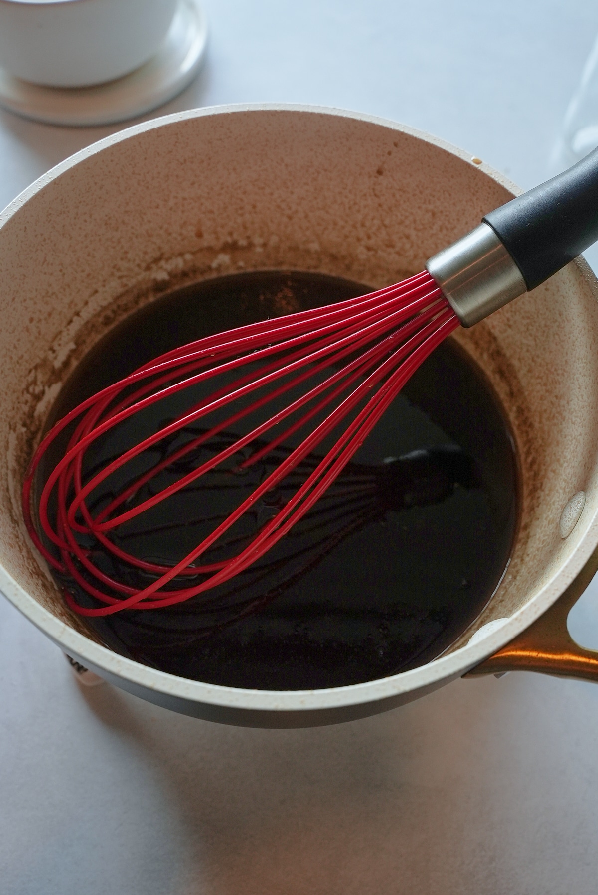 Simmering syrup in a pot with a red whisk.