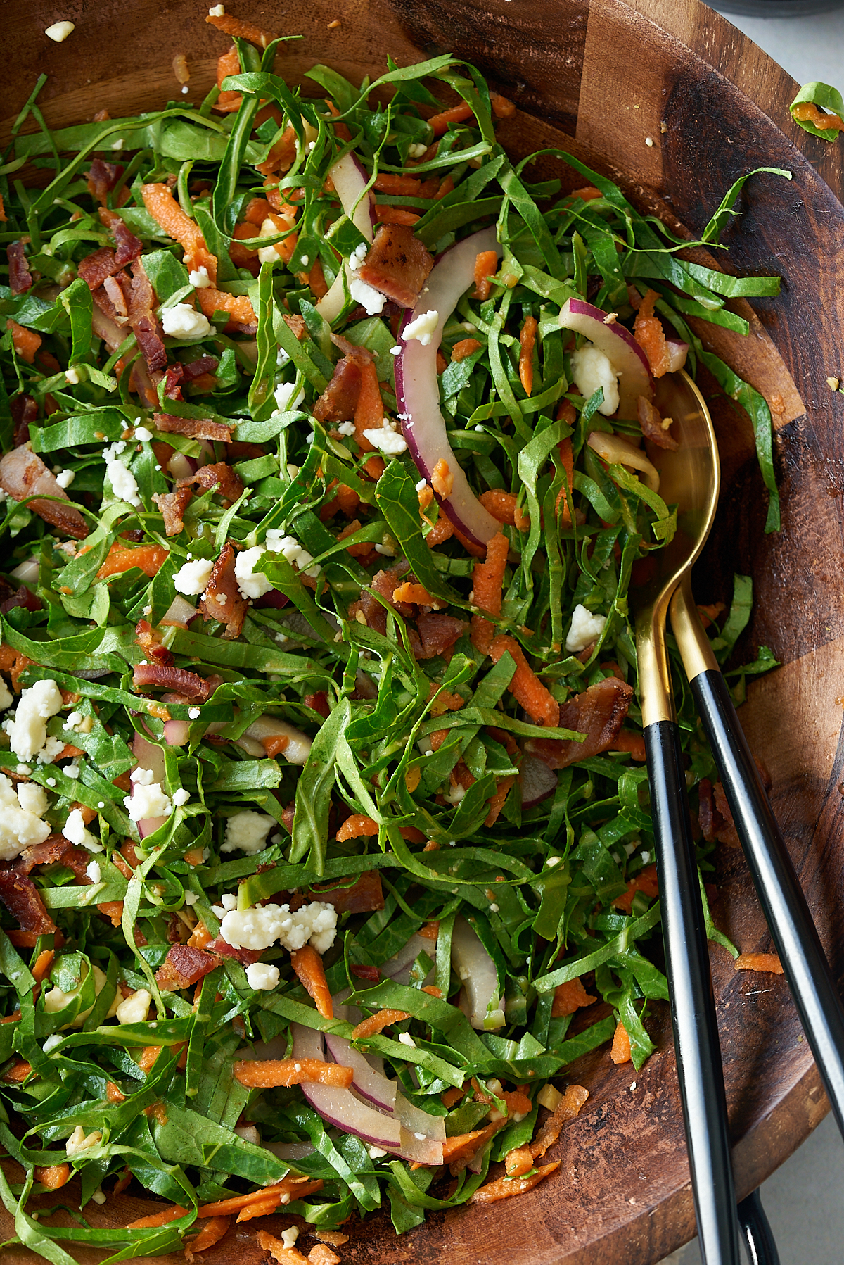 A large wooden salad bowl of freshly dressed collard green salad with salad servers.