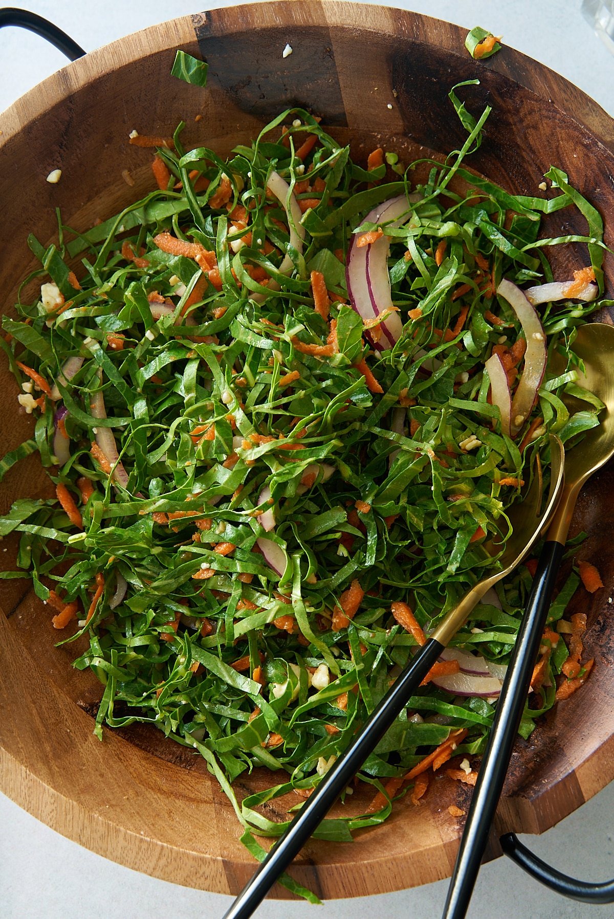 A large wooden salad bowl of freshly dressed collard green salad with salad servers.