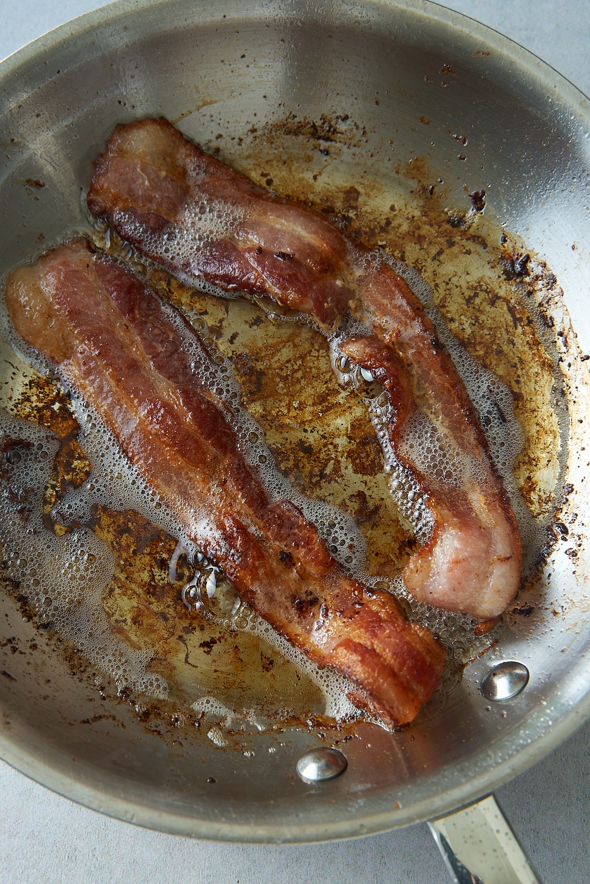 A skillet with two strips of bacon cooking in rendered bacon fat.