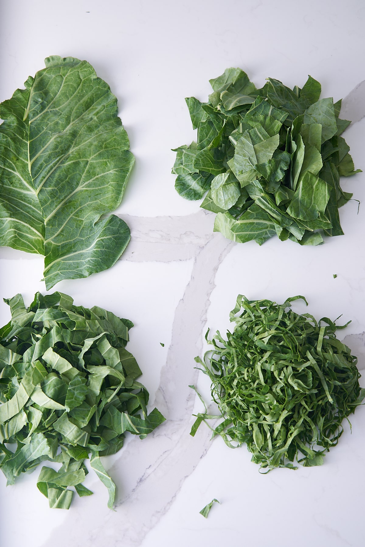 collard greens on white marble countertop. whole leaves, chopped leaves, and sliced leaves