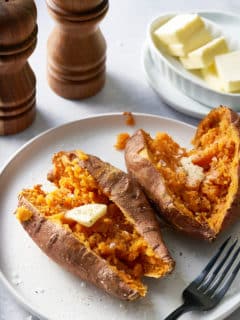 Two sweet potatoes cut open on a white plate.