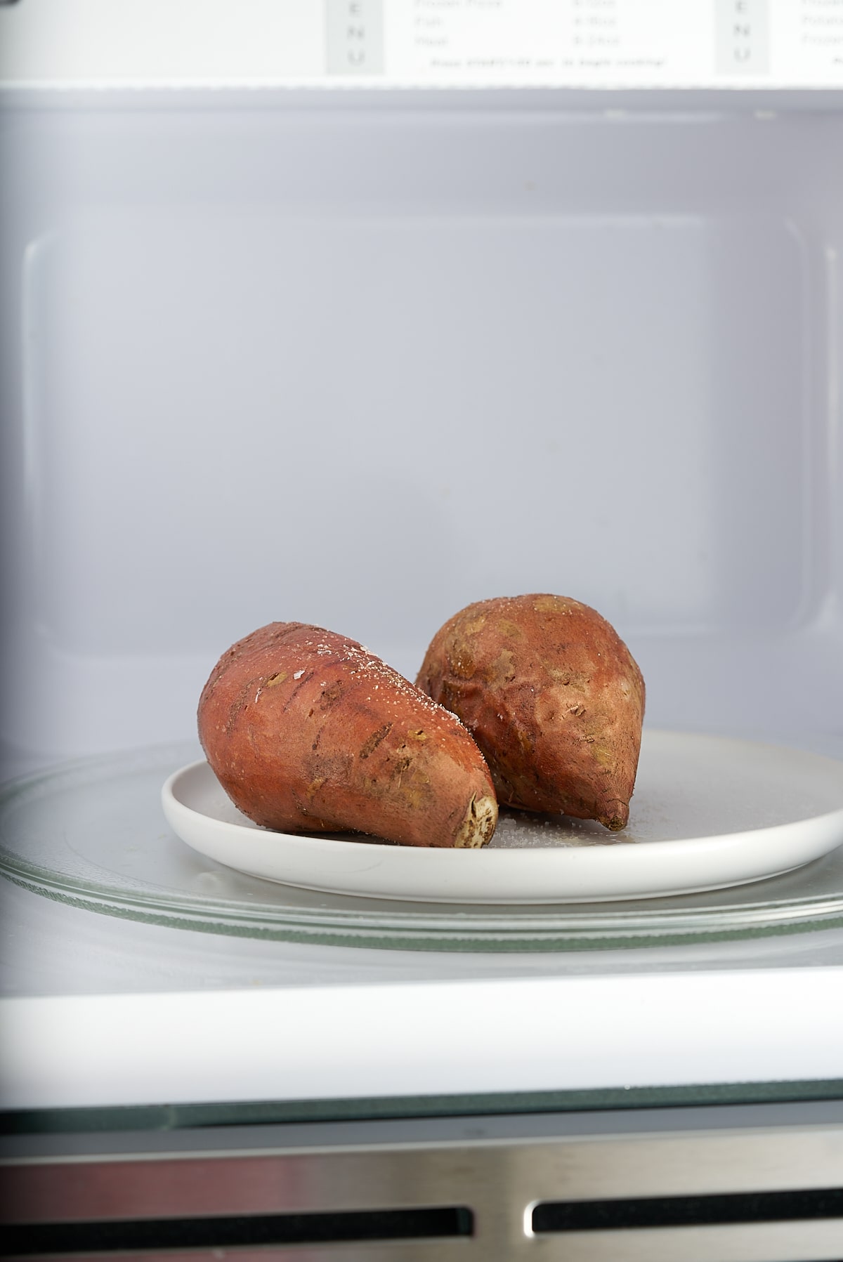 Two sweet potatoes on a plate in the microwave.