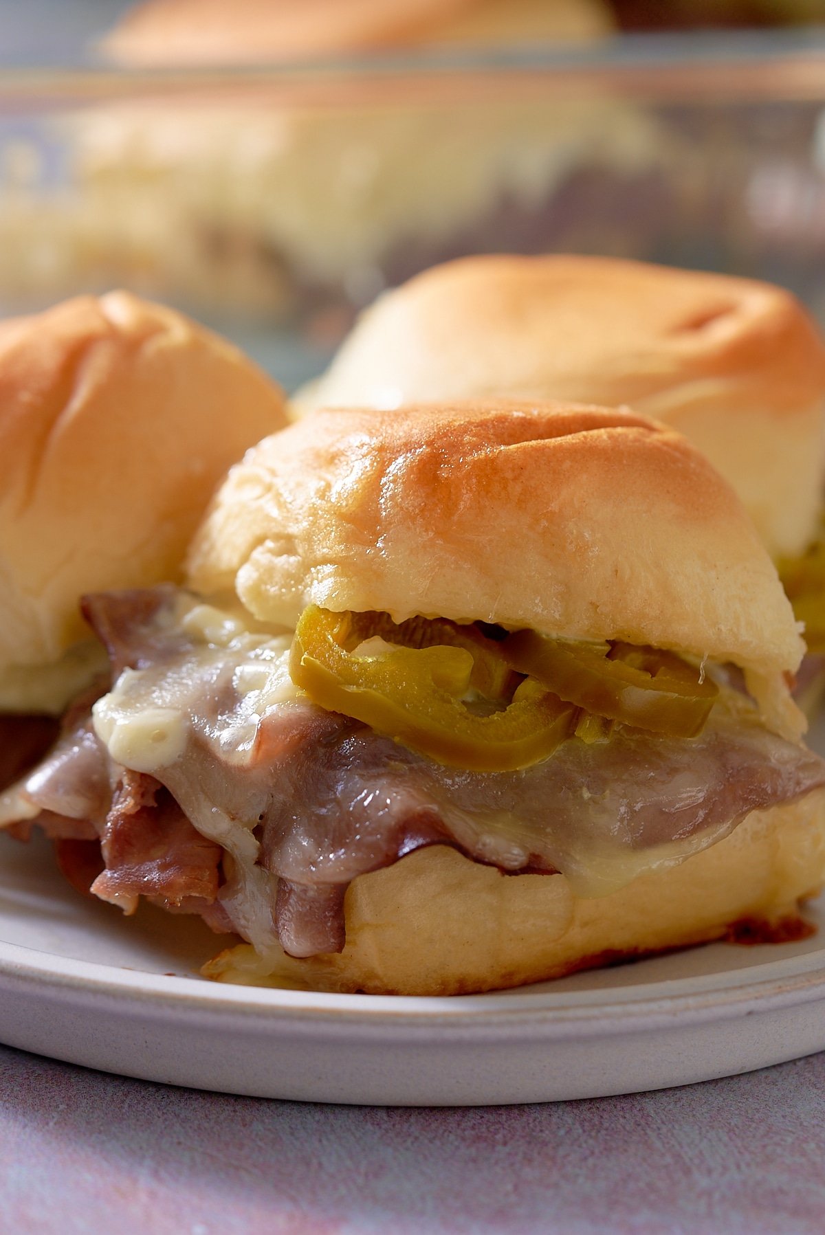 Close up of 3 toasted roast beef sliders on a white plate.