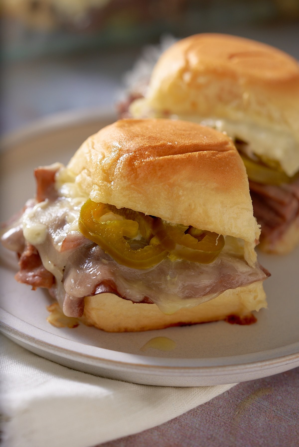 Close up of 2 toasted roast beef sliders on a white plate.