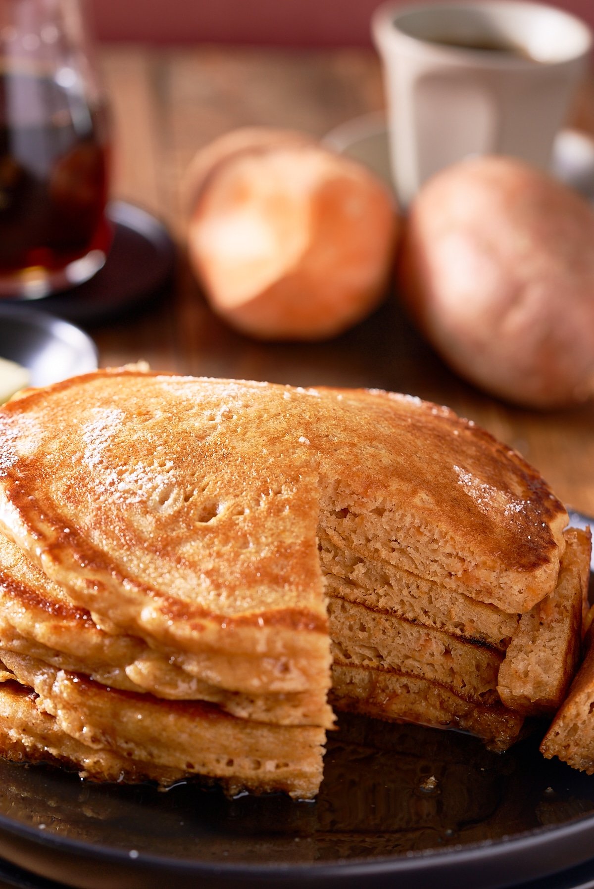 A stack of sweet potato pancakes on a black plate with a section of pancake cut out.