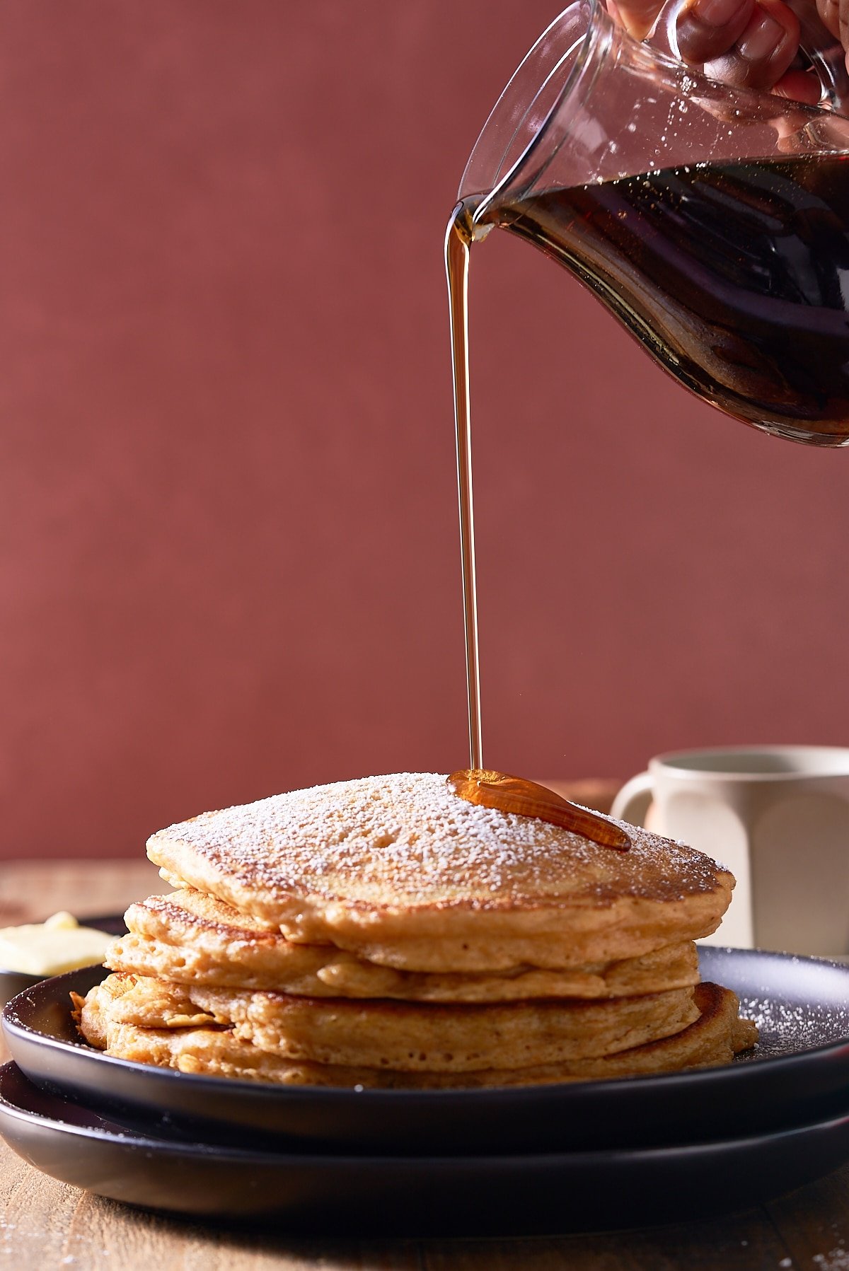 A stack of sweet potato pancakes with a jug of maple syrup being poured over.