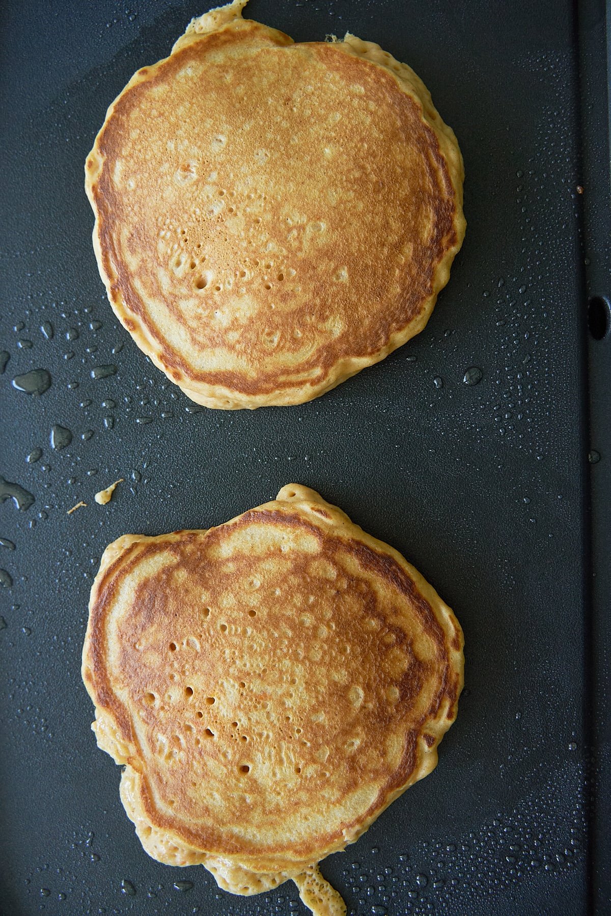 Two sweet potato pancakes on a non-stick skillet.