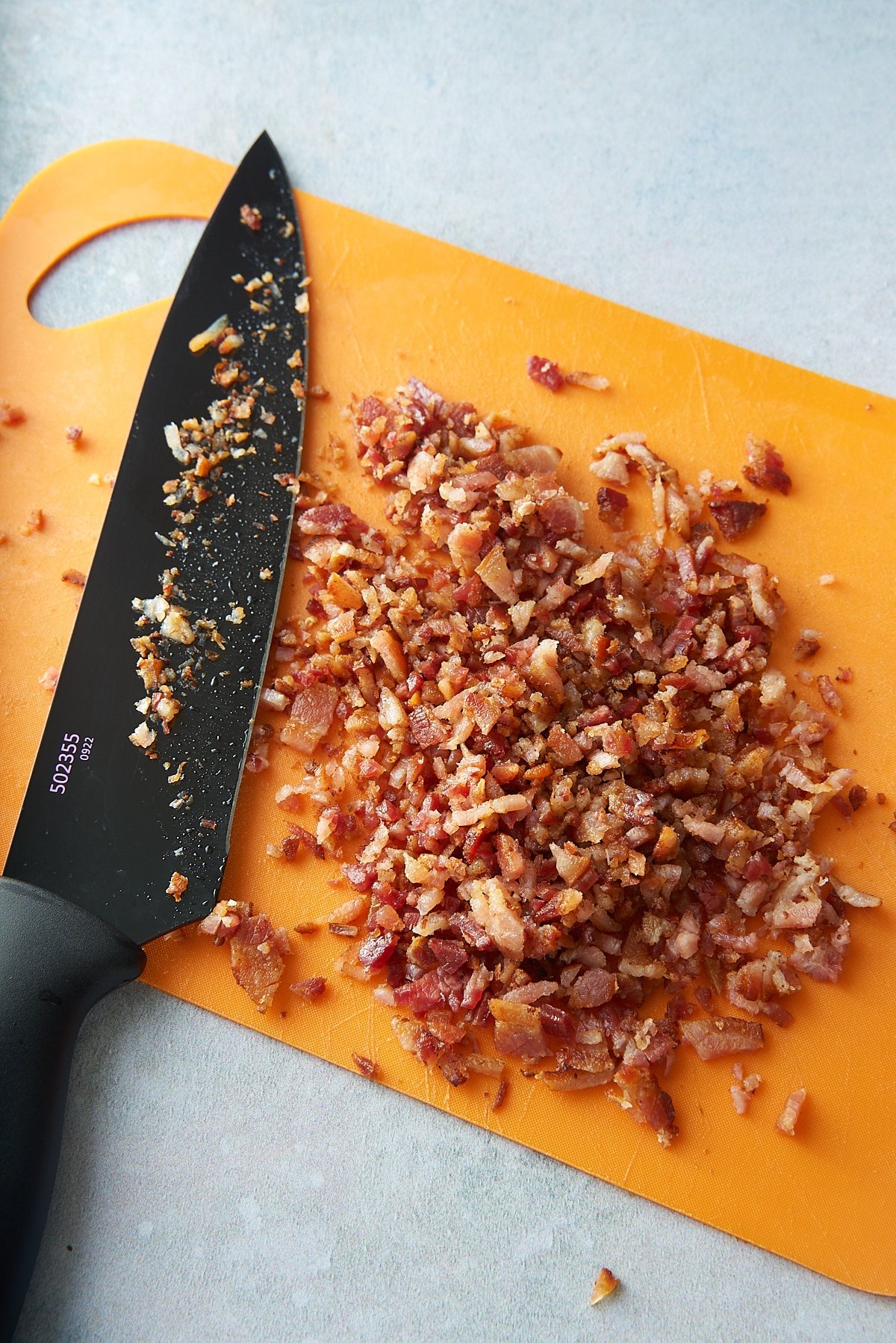 A chopping board of cooked, chopped bacon pieces, with a large kitchen knife set alongside.