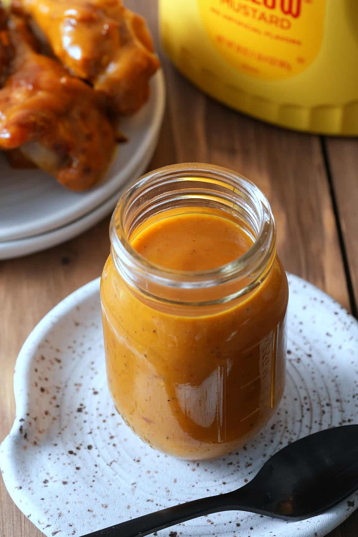 A glass jar filled with Carolina Gold BBQ sauce, with a dish of grilled chicken set alongside.