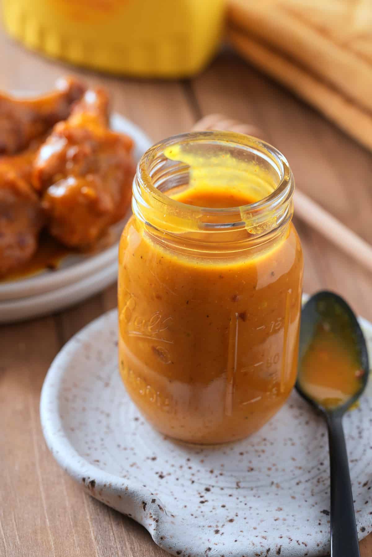 A glass jar filled with Carolina Gold BBQ sauce, with a dish of grilled chicken set alongside.