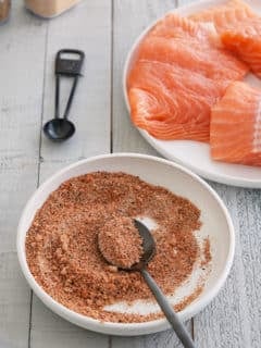 A bowl of salmon seasoning with a plate of raw salmon filets set alongside.