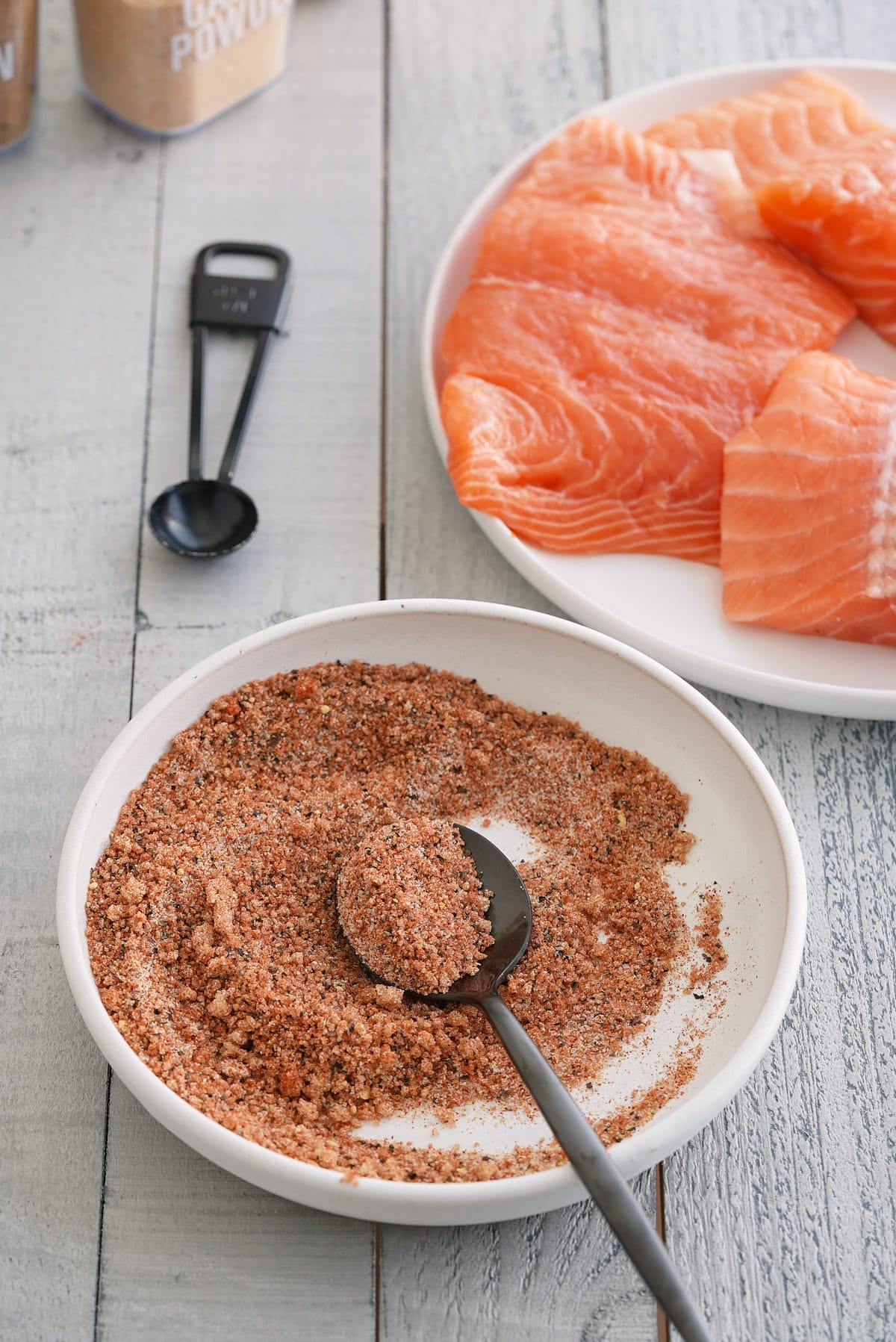 A bowl of salmon seasoning with a plate of raw salmon filets set alongside.