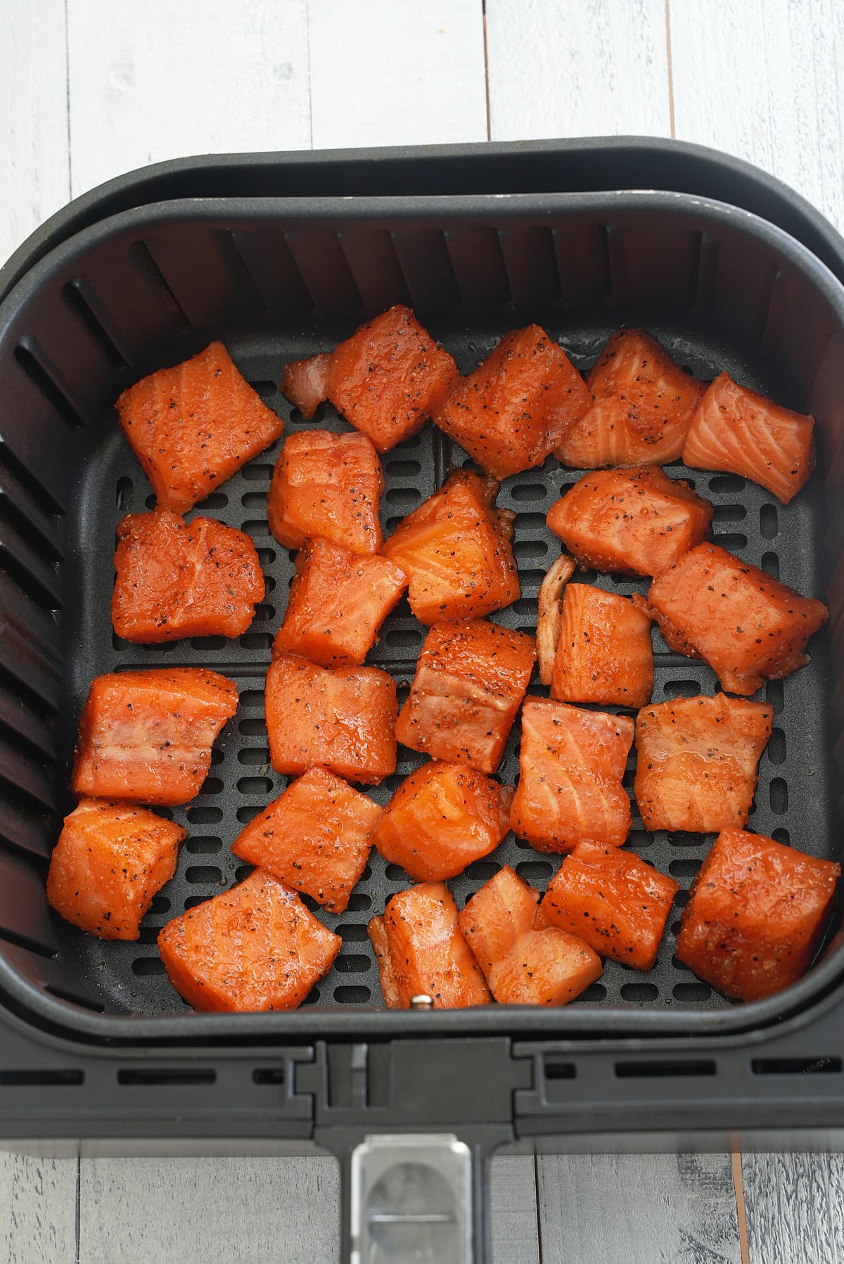 Air fryer basket filled with cubes of raw salmon coated in seasoning.