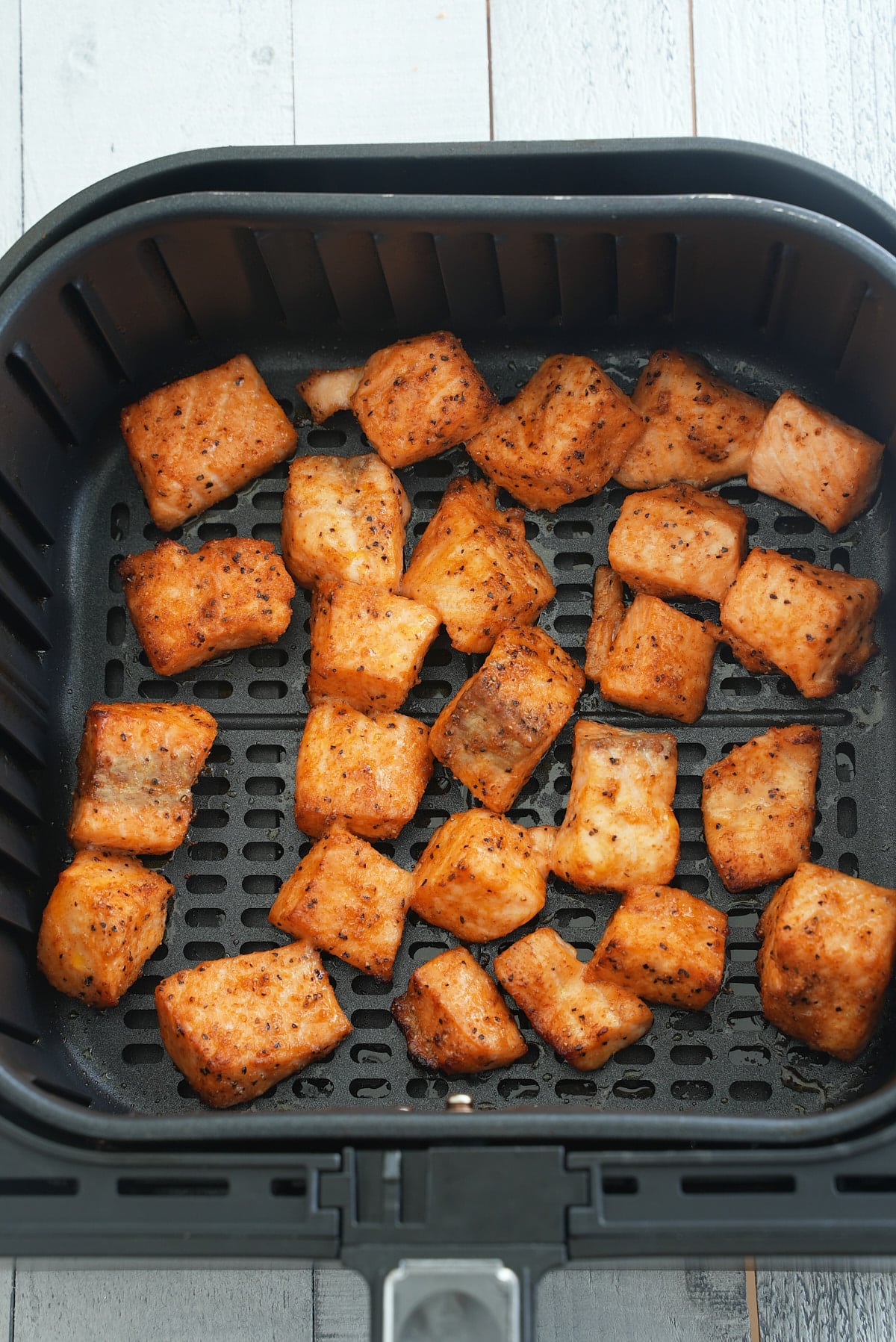 Air fryer basket filled with cubes of cooked salmon seasoned in dry salmon rub.