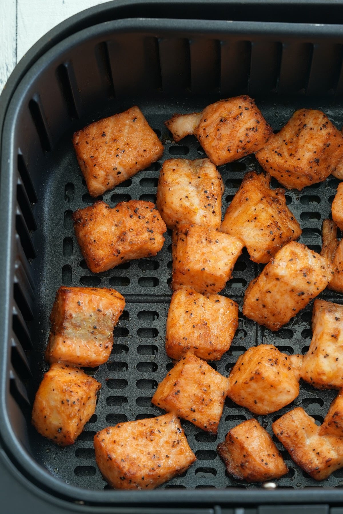 Air fryer basket filled with cubes of cooked salmon seasoned in dry salmon rub.