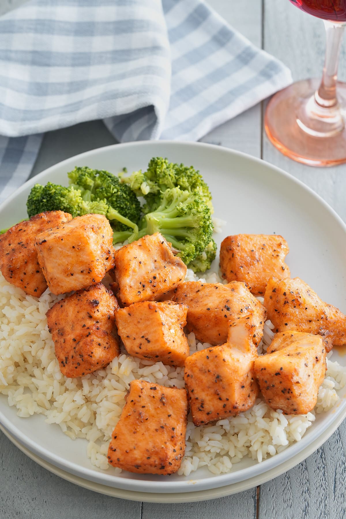 A white bowl of steamed white rice topped with salmon bites and a side of steamed broccoli.