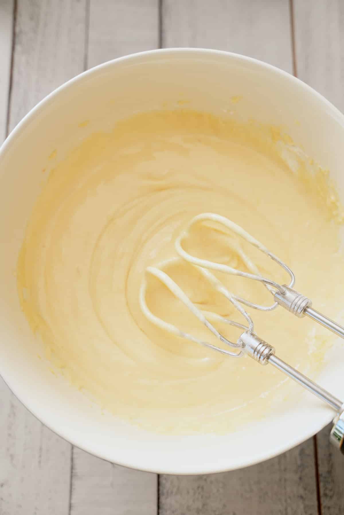 White bowl filled with yellow cake mix, eggs, oil and sour cream whisked together.