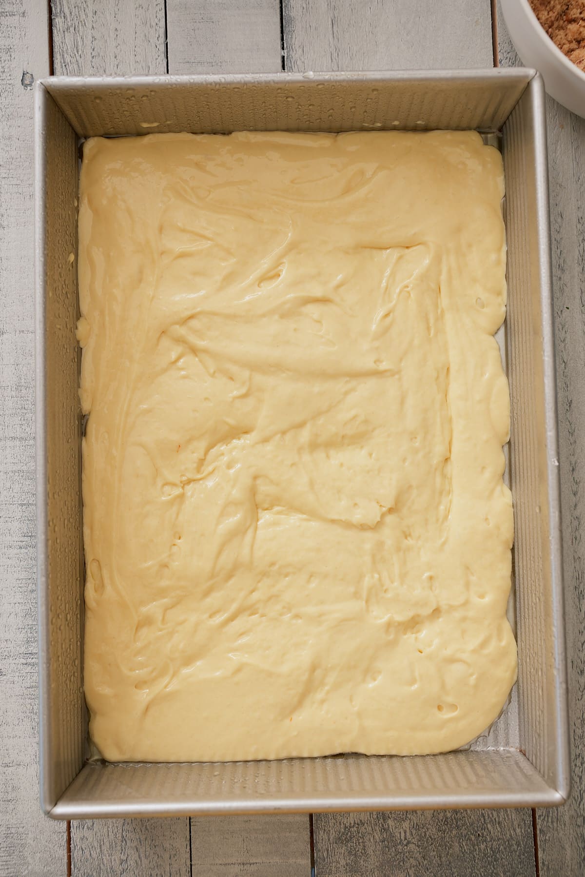 Yellow cake mix batter spread across the base of a rectangular cake tin.