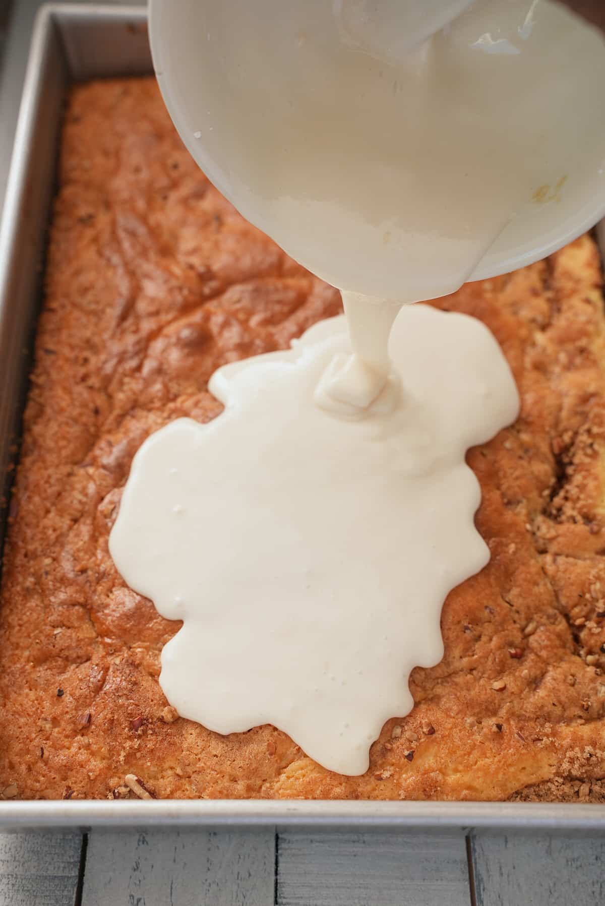 White glaze being poured over cake.