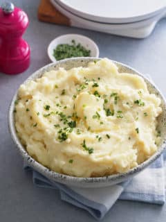 A bowl of microwave mashed potatoes topped with butter and garnished with freshly chopped chives.