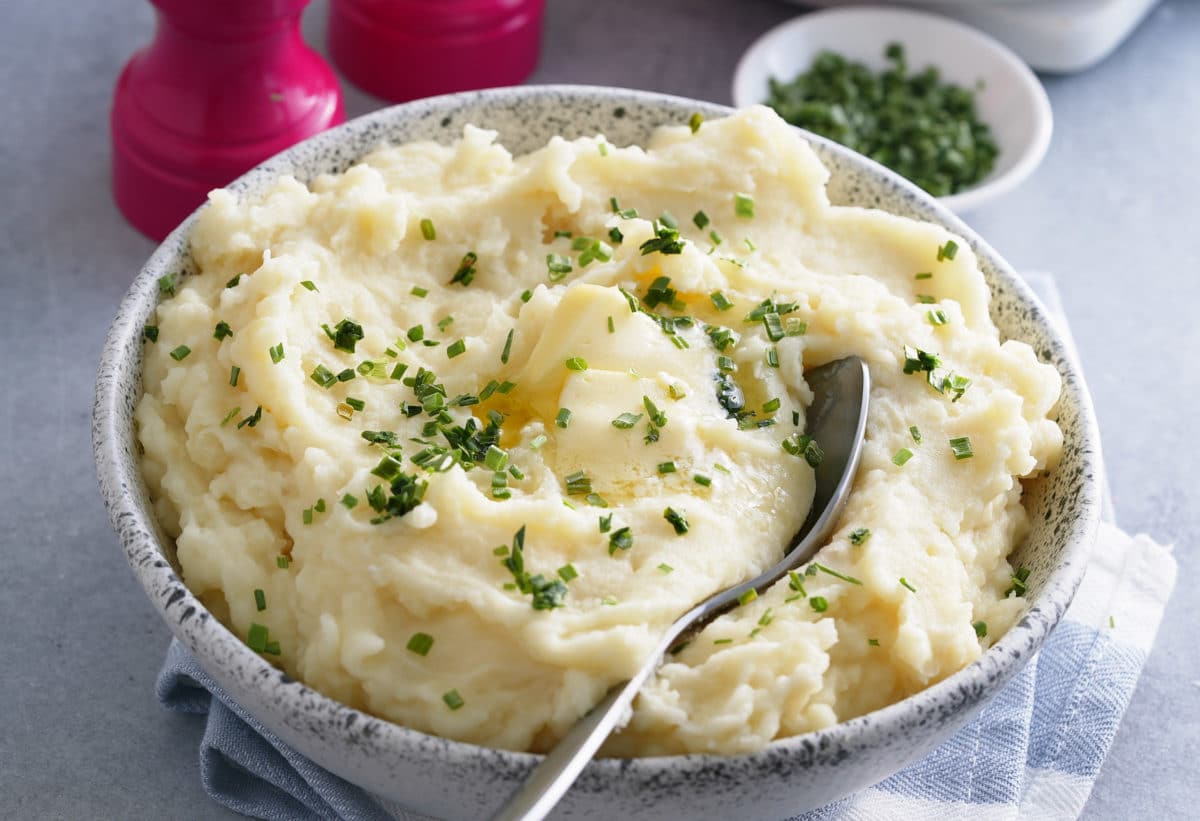A bowl of microwave mashed potatoes topped with melted butter and garnished with freshly chopped chives.