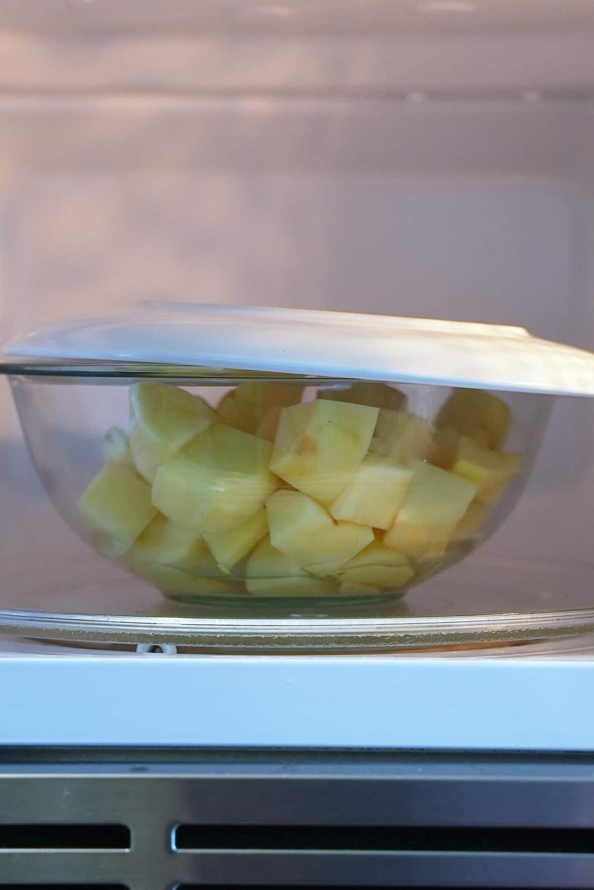 A glass bowl filled which chopped potatoes in the microwave with a plate set on top of the bowl.