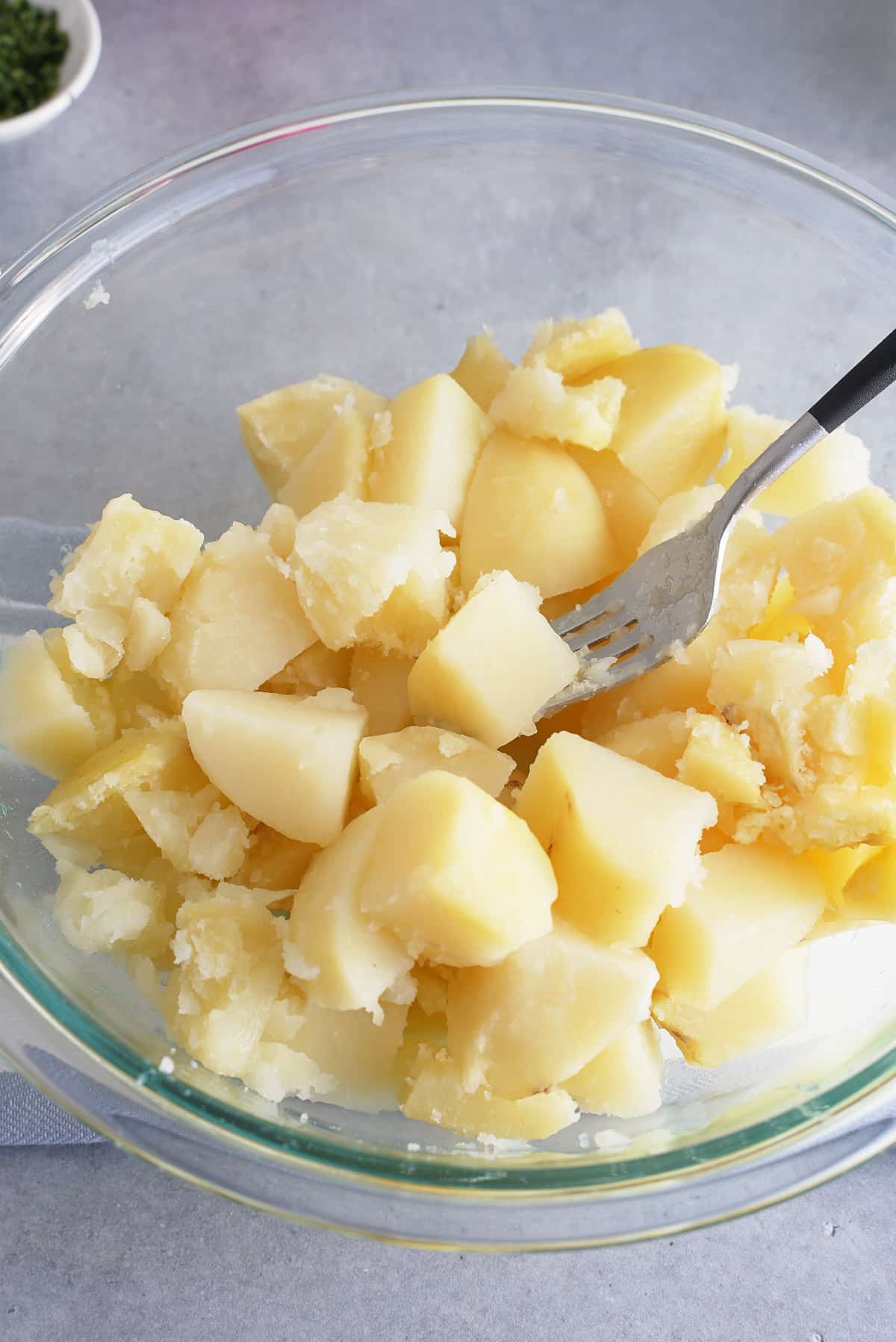 A glass bowl filled with chunks of cooked potato.