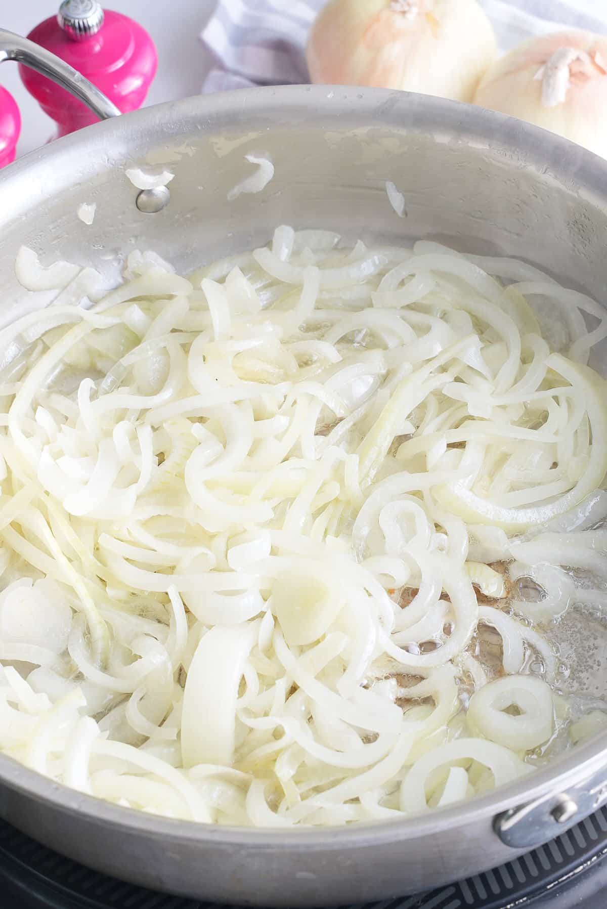 A large skillet with sliced onions being cooked in butter.