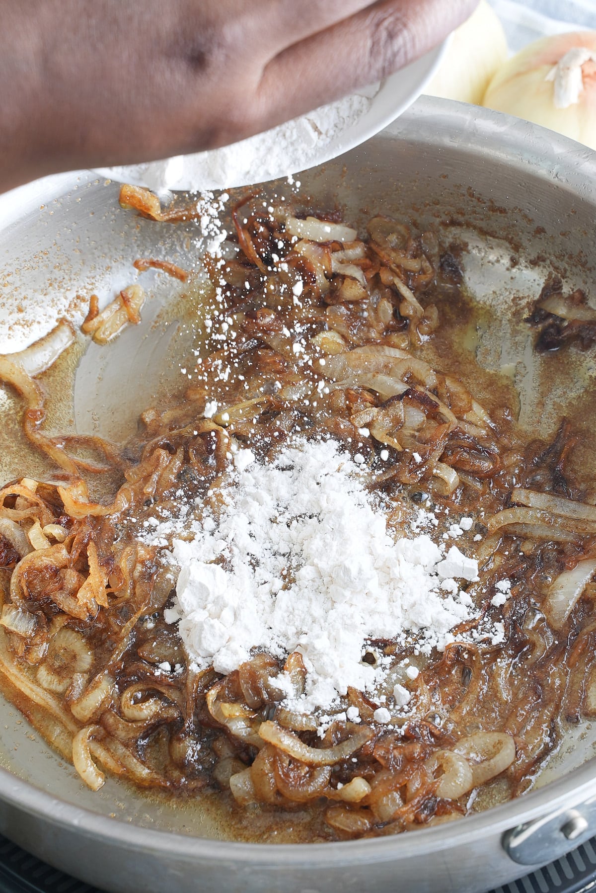 A large skillet of cooked onions with flour being added.