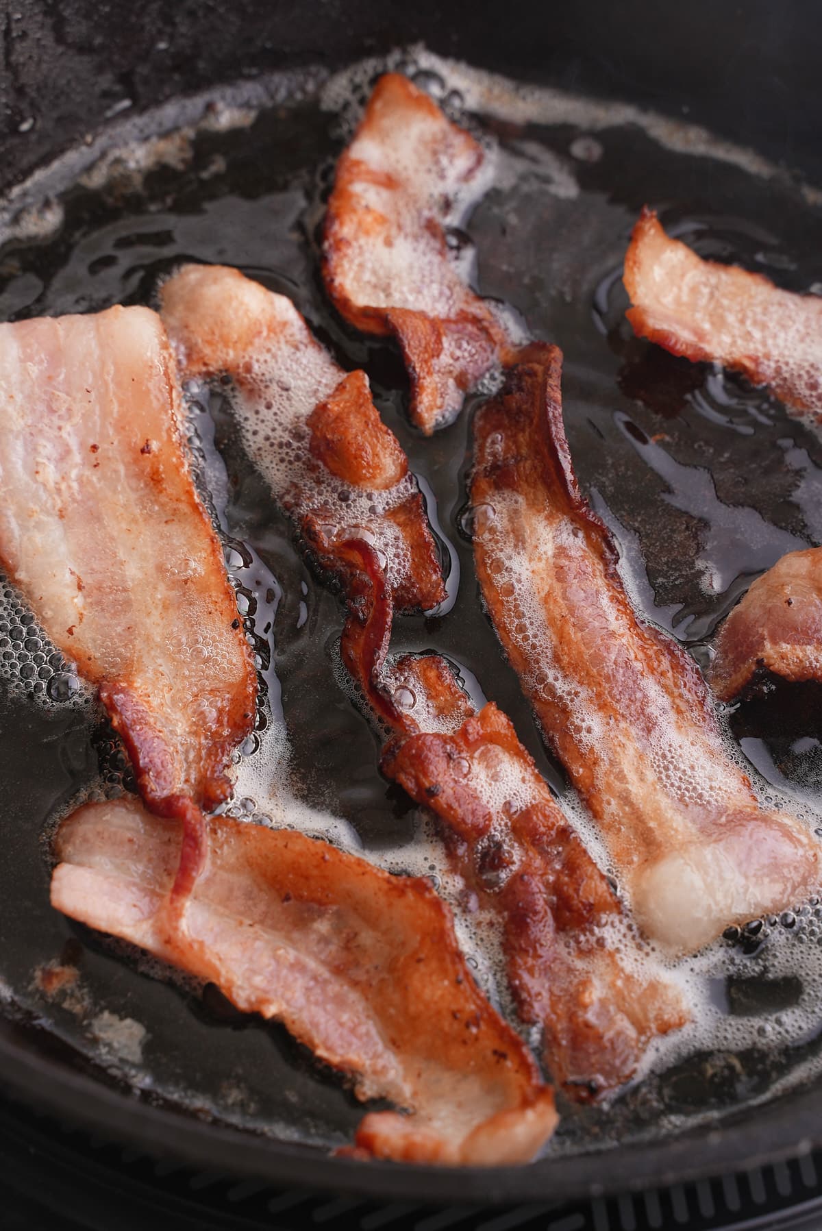Frying pieces of bacon in a skillet.