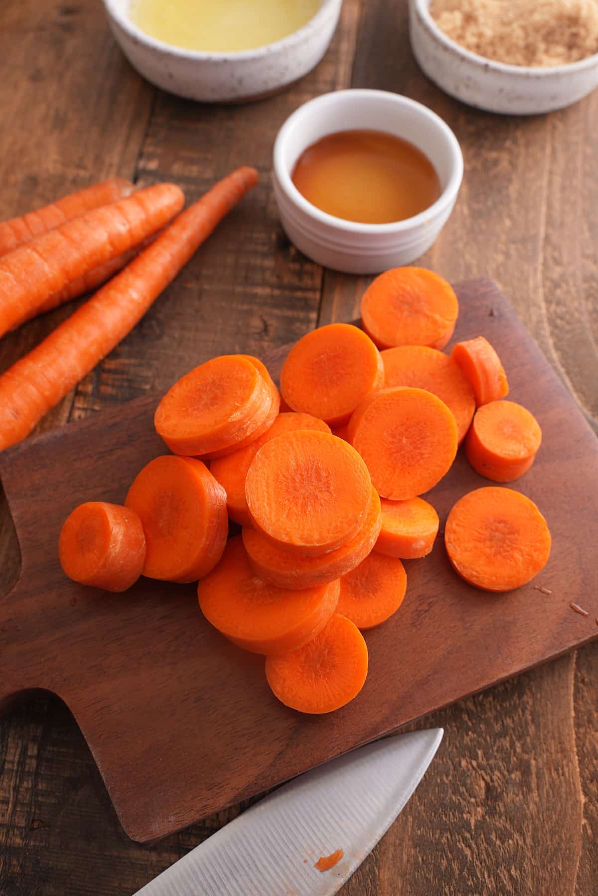 Sliced carrots on a wooden cutting board with whole carrots set alongside.