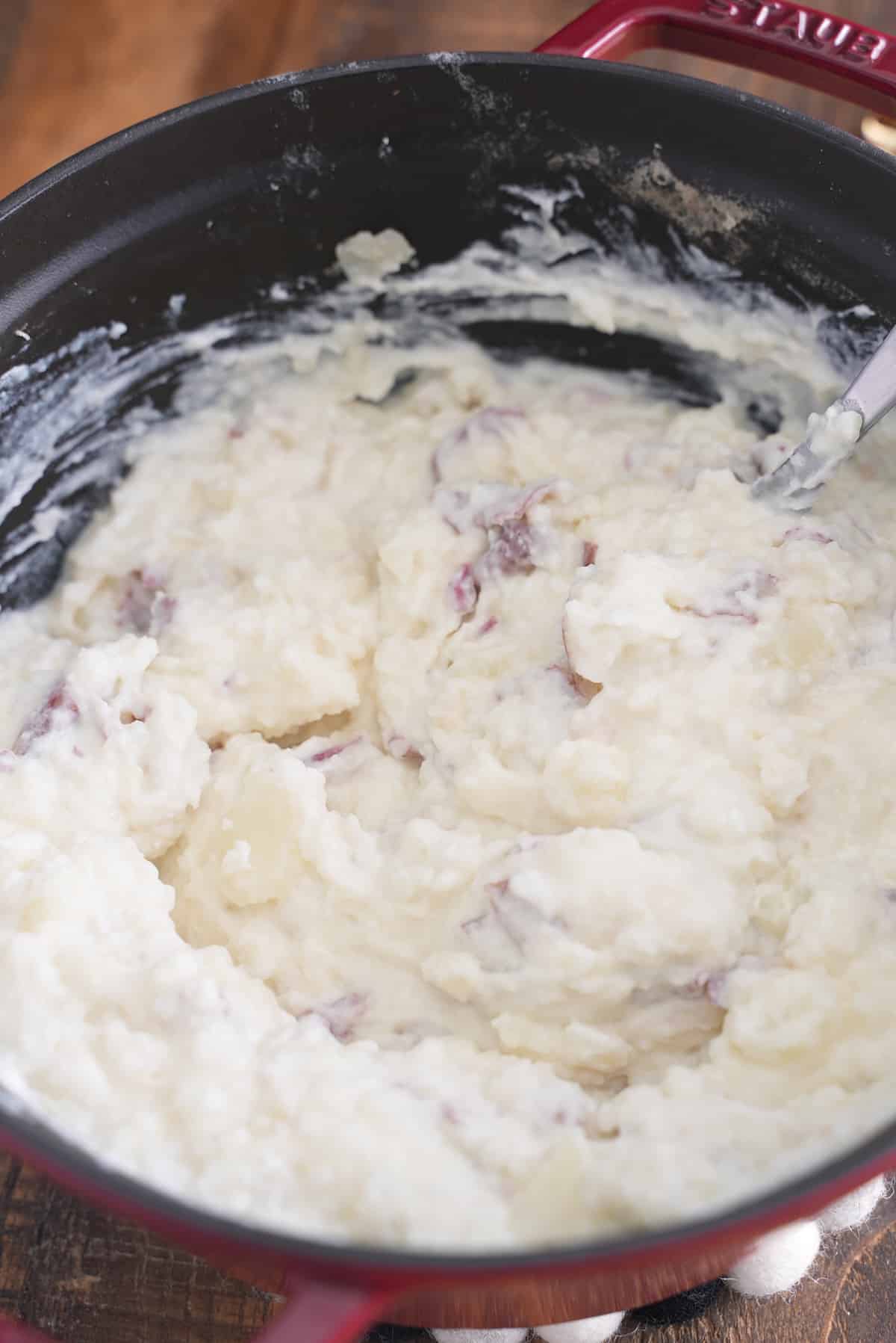 Sour cream being stirred through red skinned mashed potatoes.
