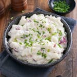 A bowl of mashed red skinned potatoes garnished with finely chopped chives.