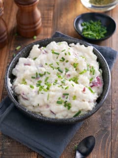 A bowl of mashed red skinned potatoes garnished with finely chopped chives.