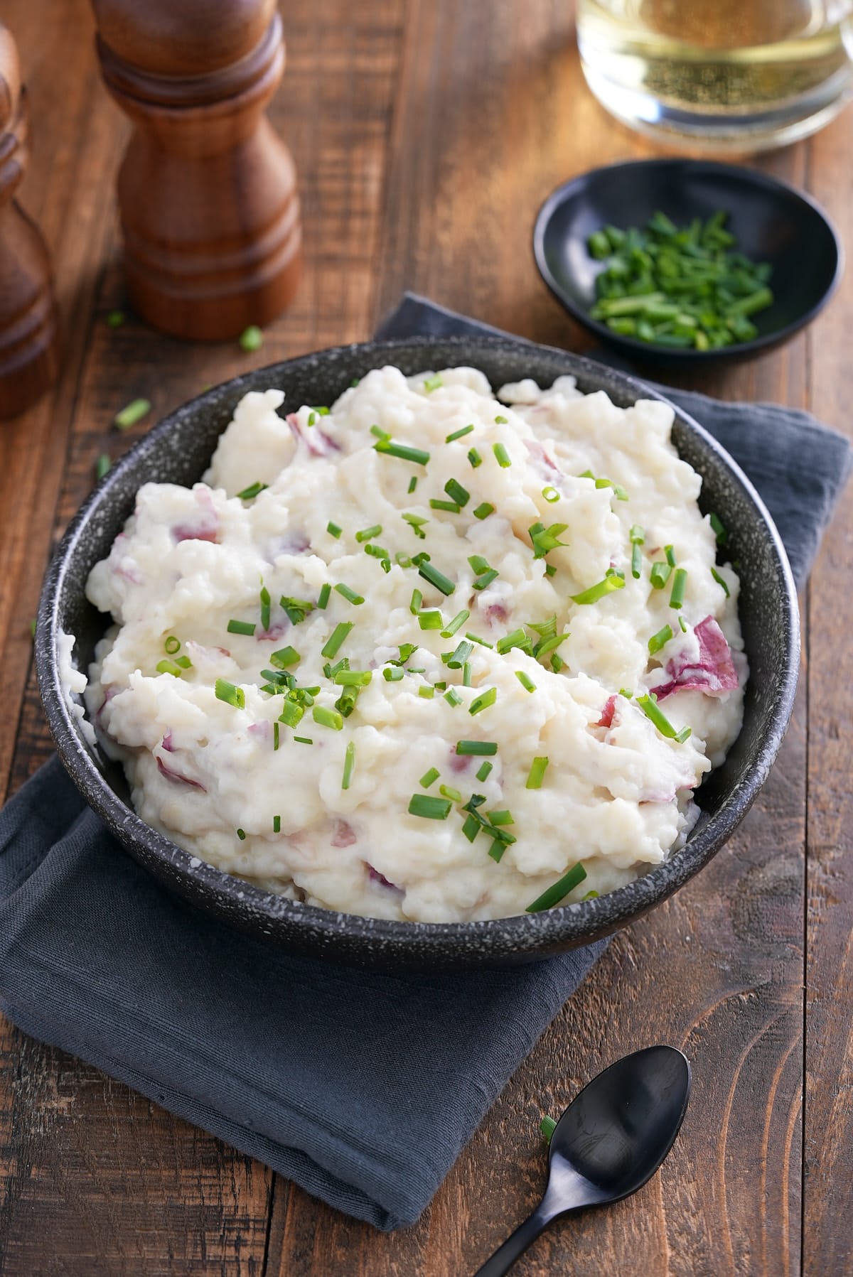 A bowl of mashed red skinned potatoes garnished with finely chopped chives.